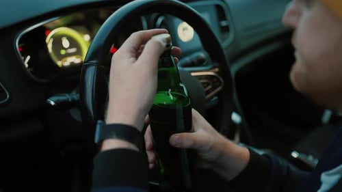 Unrecognizable Man Driver Sitting in Car with Beer Bottle and Lid in Hands