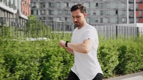 Man Jogging in Urban Setting Checking Smartwatch