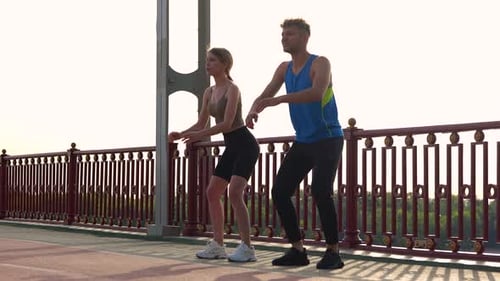 Camera Approaching Young Couple of Man and Woman in Sportswear Working Out Outside on the Bridge