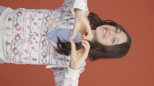 Young Woman Makes Heart Shape With Hands and Smiles