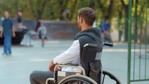 Shot Back Depressed Man Sitting on a Wheelchair Look at Playground in Park Feel Sad Paralyzed