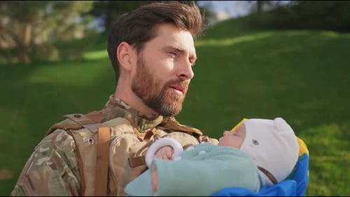 Soldier Holding Sleeping Infant Outdoors in Daytime