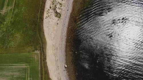 4k aerial top down of coast line with green field and cliff right at the calm ocean on a summer day