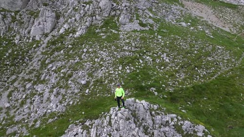 A man stands on a mountain peak and a drone flies around him. Aerial view.