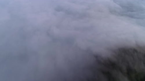 A 4K drone shot above low-lying clouds, flooding over mountain tops and down into a valley, near Dav