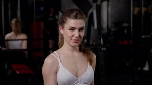 Confident Female Athlete Engaging in Bicep Curl Exercises with a Focused Expression in a Gym Setting