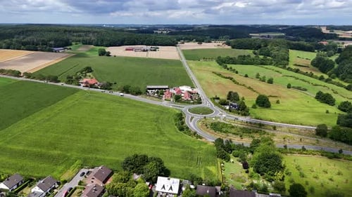 Aerial establishing shot of rural farm fields and new roundabout in suburbia of town. Sunny summer d