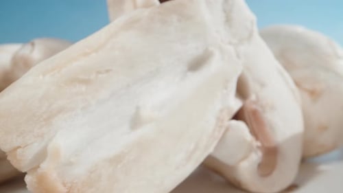 une poignée de champignons tranchés sur une table blanche, la caméra les traverse sur fond bleu