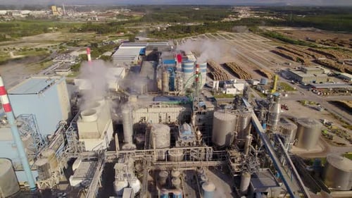 Aerial orbit shot of a big industrial plant on a sunny day - a lot of smoke comes out of the chimney