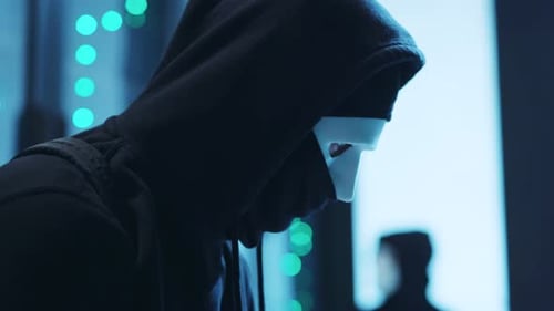 Masked Hacker Typing on Laptop in Data Center
