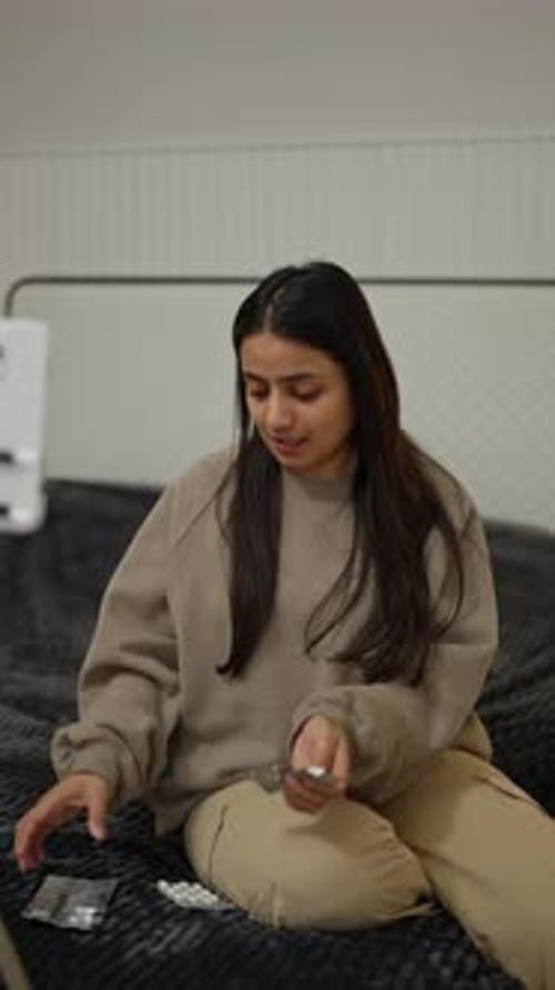 A Happy Brunette Indian Girl in a Gray Sweater Sits on the Bed and Blogs About Medicine for Her