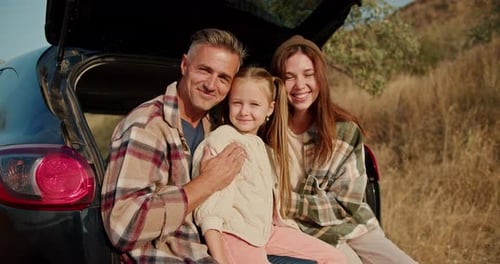 Portrait of a Happy Family Who During Their Picnic Outside the City Sits in the Open Trunk of a