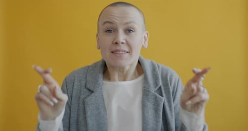 Slow Motion of Young Woman Making Wish Then Crossing Fingers and Praying on Yellow Background