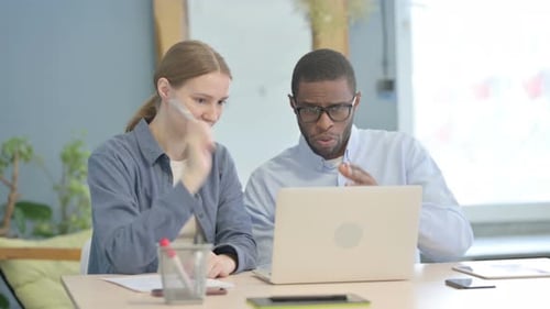 Adults Work Together at Desk on Laptop