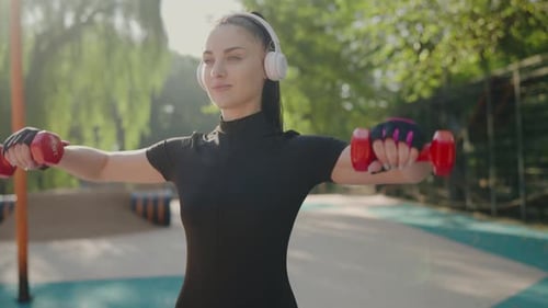 Fit woman lifting dumbbells outside in the sunlight