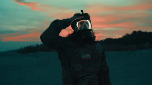 Man Wearing Gas Mask Stands on Beach at Sunset