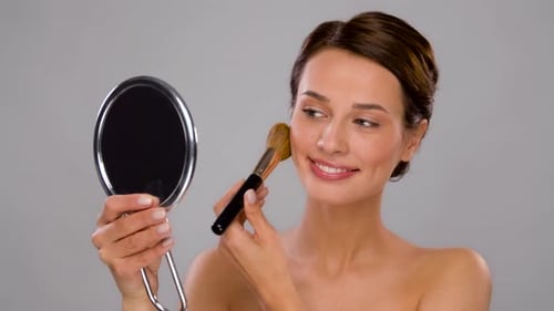 Woman Applying Makeup with Brush Looking in Mirror