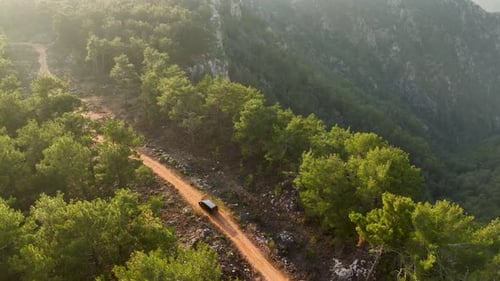 A Black Car Rides on a Mountainside Surrounded By a Lush Green Forest Aerial View Perfect Background