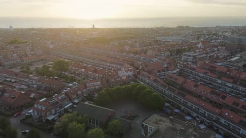 Aerial sunset view over a Dutch coastal town with rows of red-roofed houses, tree-lined streets