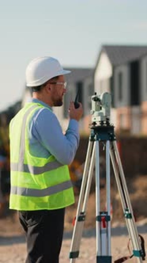Construction Worker Using Walkie-Talkie by Theodolite on Construction Site