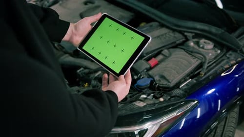 Male car service worker with a tablet in his hands on which there is a green screen near the hood