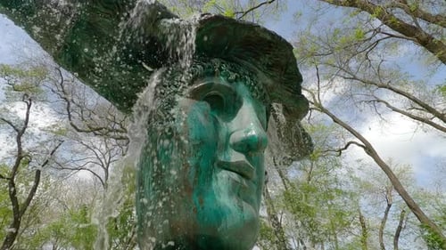 Bottom view of running water jets from bronze mask fountain, slow
