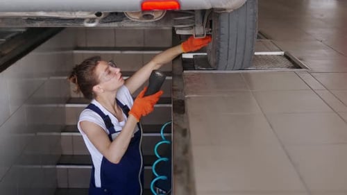Female Mechanic Inspecting Car Suspension on Hydraulic Wheel Play Detector with Remote Control