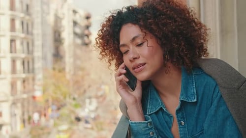 Close up of woman sitting on balcony talking on mobile phone