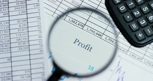 A hand with a magnifying glass passes over a financial newspaper and financial bag with a business