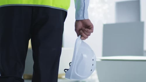 Construction Worker Walks Holding Hard Hat Indoors
