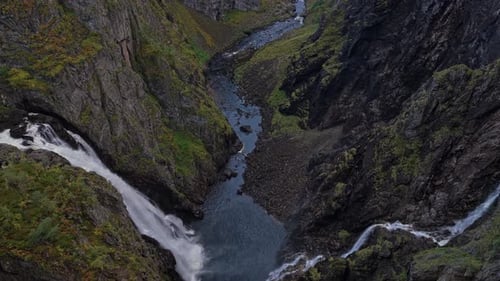 Aerial shot of waterfall pouring through rugged Norwegian landscape