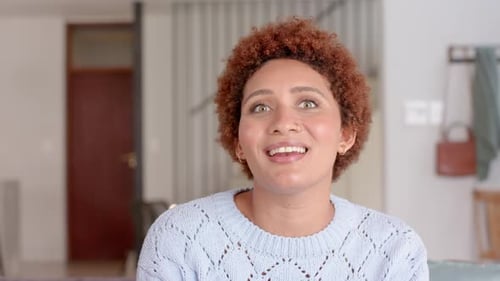 Expressing surprise, woman with curly hair gesturing with hand indoors, video call