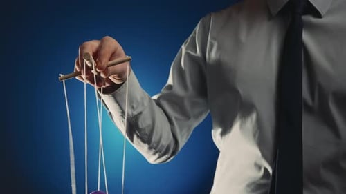 Un hombre de negocios con camisa gris y corbata negra controla una marioneta con un manipulador de madera y cuerdas