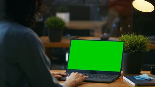 Beautiful Female Office Employee at Her Desktop Works on a Mock-up Green Screen Laptop. Over the Sh