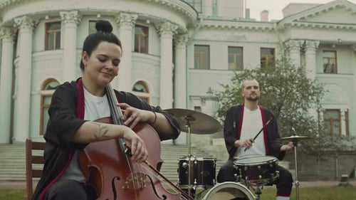 Young Woman Playing Cello and Man Drumming during Performance in Park