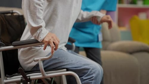 Elderly patient on wheelchair trying to stand and walk exercising with caregiver nurse at home