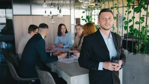 Confident Man with Team Meeting in Background