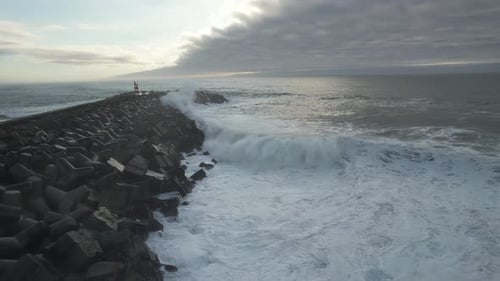 Waves Crashing Against Rocky Pier with Lighthouse