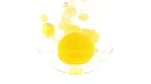 Yellow Oil Droplets Falling Into Water in Glass