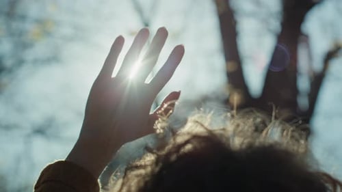 Nahaufnahme einer Frau mit erhobener Hand, die in die Sonne blickt. Aufgenommen mit RED-Heliumkamera in 8K
.
