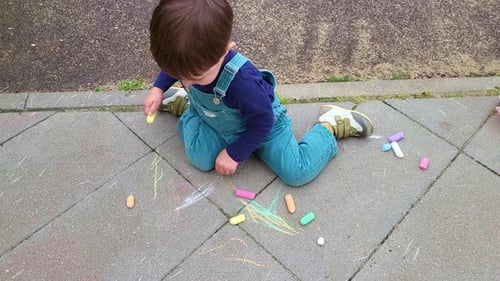 Baby is sitting and drawing with crayons on a tile near the playground. Baby aged two years (two-yea