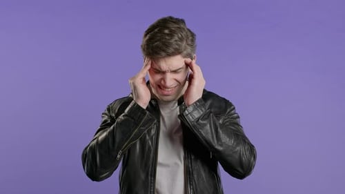 Man Rubbing Temples in Discomfort on Purple Background