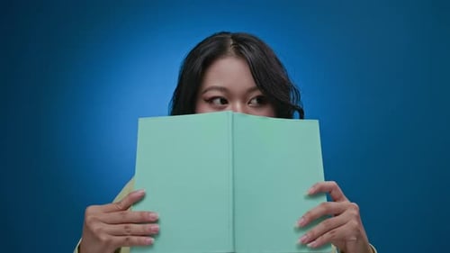 Woman Peeking Over Book, Smiles at Camera