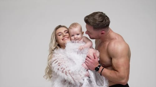 Happy family of three in the studio. Lady waves her child and father kisses his baby boy.