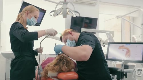 Dentist and His Assistant in Protective Masks Treat a Patient's Teeth in a Dental Clinic Healthcare