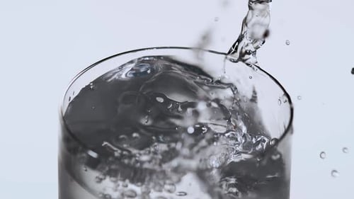 Ice Dropping into Clear Liquid Creating Splashes and Bubbles