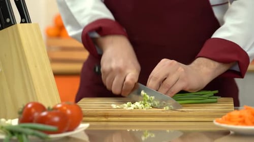 Professional chef chops green onions on a cutting board. Chefs hand chopping up scallions.