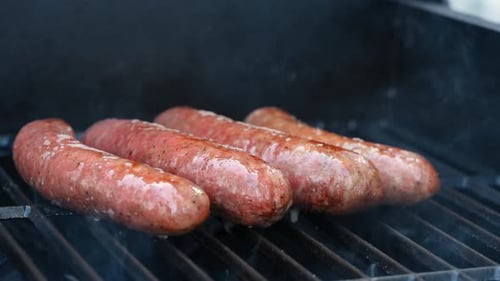 Blick auf rohe Würste, die auf dem Grill mit offener Flamme grillen, Nahaufnahme von saftigem Fleisch, das auf dem Grill zubereitet wird