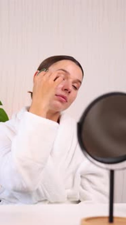 woman applying face sheet mask at home, cream or serum and massaging skin with roller.