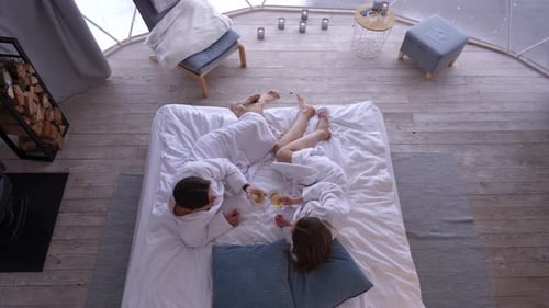 Top View Happy Couple Clinking Glasses Drinking Champagne White Wine Lying on Bed Indoors